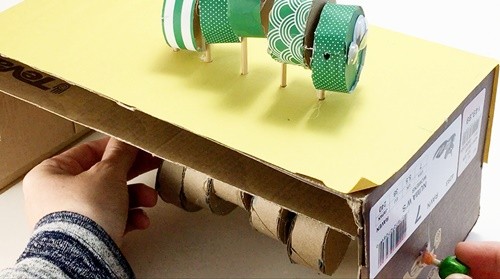 Sideview of the automaton with the axle just sticking out of a side panel. A bead is being glued on.