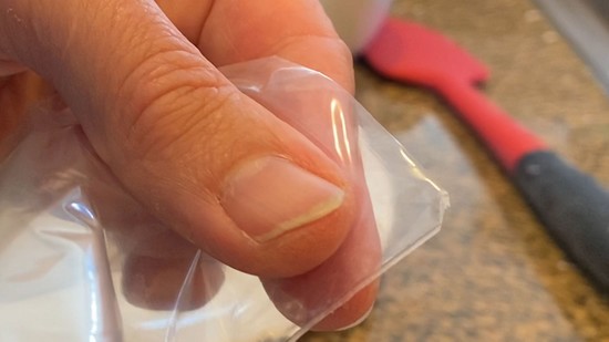 A bottom corner of a resealable plastic bag with a small tip cut off. The cut-off tip is about 2 millimeters wide.