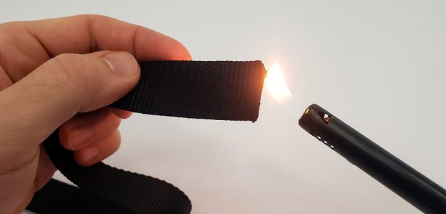 A lighter held up to the end of strap with the flame just touching the end. 