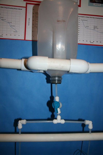 An upside plastic bottle drains into a T-shaped valve that splits the water into two separate streams