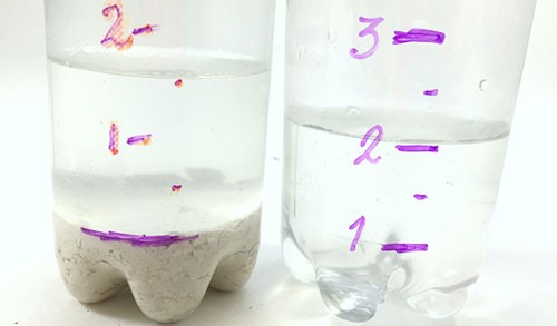 A plastic bottle filled with water and sand on the left and another without sand on the right