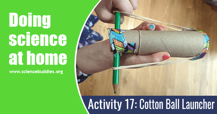 Student hands holding finished cotton ball launcher from toilet paper tube, rubber bands, and a pencil