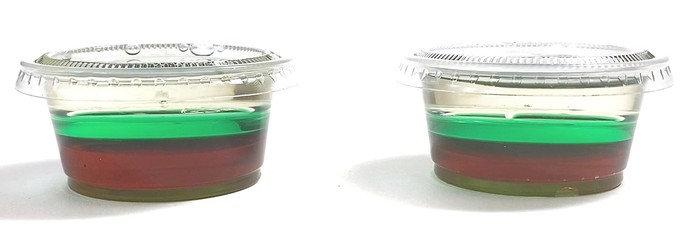 Two mini cups each filled with three different liquids that separate into a brown, a green, and a yellow layer.