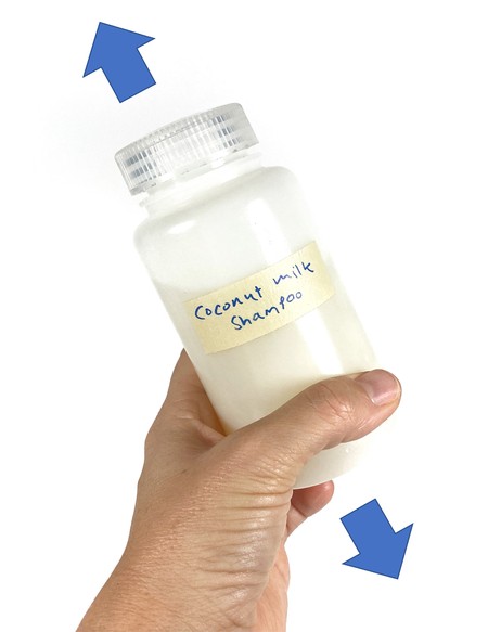 A hand holding a bottle filled with liquid and a piece of wool yarn. Arrows point up and down from the bottle.