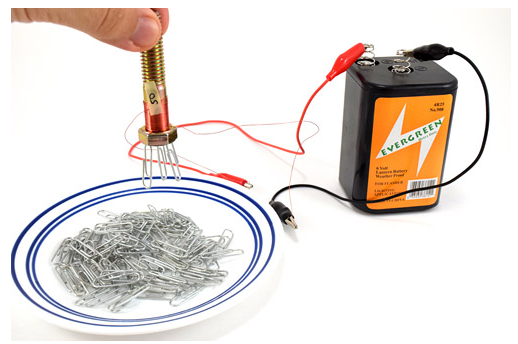 An electromagnet made of wires, a bolt and a battery hovers over a plate of paperclips