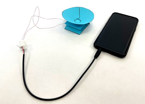 Paper speaker connected to cell phone by wires and audio cable.