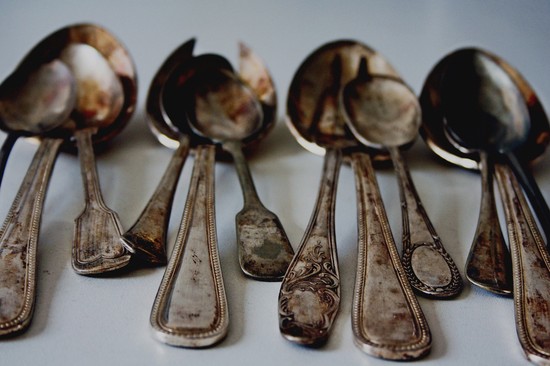 Twelve tarnished silver spoons appear dull and dirty.