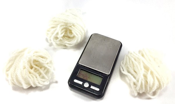 Three pieces of wool yarn lying next to a digital scale.
