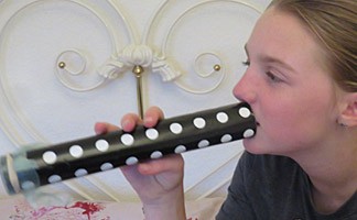 Young woman blows into a homemade kazoo made from a cardboard tube