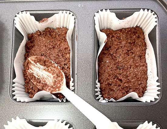 A wet, red-brown mixture filling paper muffin liners in a pan one-third full.