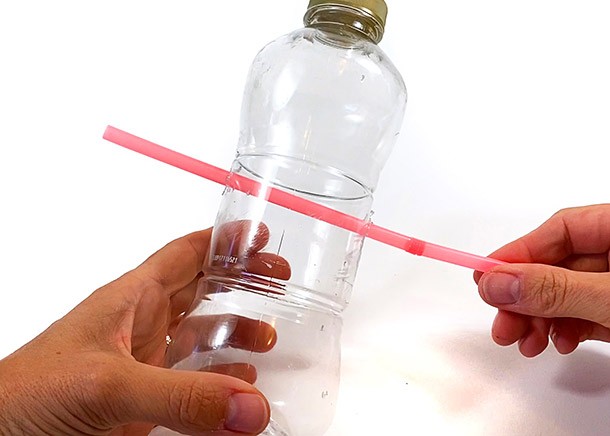 A plastic bottle with a straw sticking through two holes in the sides of the bottle.