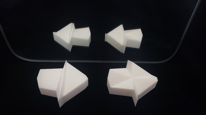Two versions of the 3D printed impossible arrow that use different triangulation methods for their top surface. One connects triangles across the shape to opposite edges, and one connects triangles to a central point. Both arrows appear to point to the right while their reflection ns in a mirror appear to point to the left. 