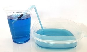 A straw siphoning water from a plastic cup into a shorter plastic container.