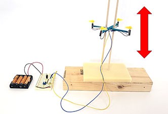 A miniature drone flying up and down on guide poles, connected to an altitude control circuit.