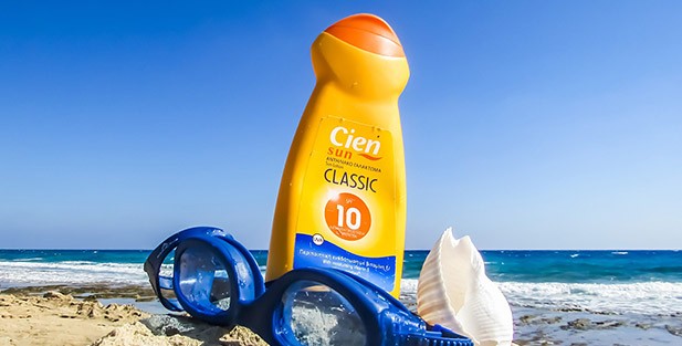Sunscreen lotion and swimming goggles on the beach on front of the ocean.