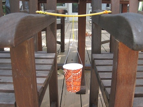 A beam made of spaghetti suspended between two chairs holding a weight