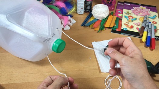 Yarn threaded through holes at the top of a plastic jug