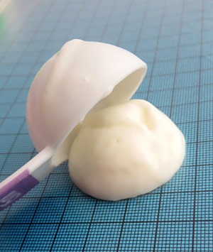 A white solid is transferred from a tablespoon onto a blue sheet of graph paper