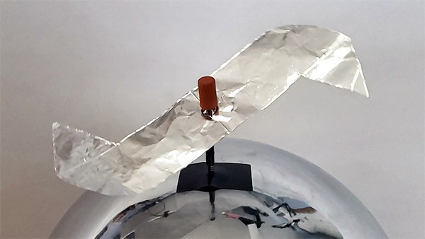 An aluminum foil propeller with pointed tips, mounted on a nail that is attached to the dome of a Van de Graaff generato