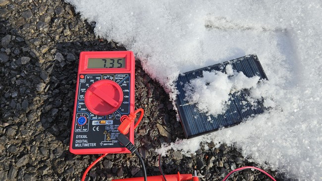 small solar panel with partial snow cover connected to multimeter