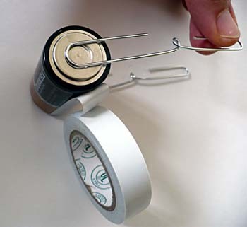 Two paperclips are taped to the top and bottom of a C cell battery parallel to each other