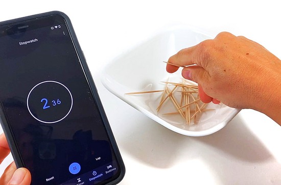  A hand reaching into a bowl filled with toothpicks. A stopwatch next to the bowl shows 2 seconds. 