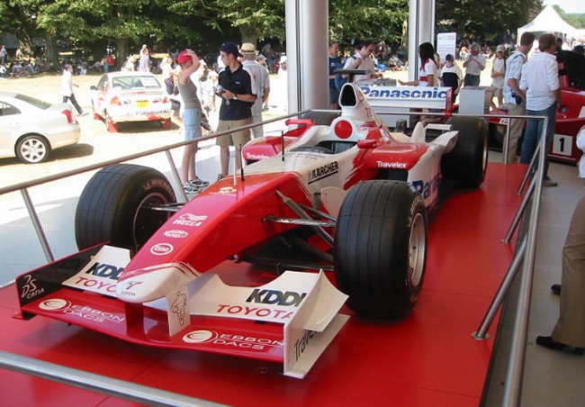 A formula one race car on a display stand. The car is very low to the ground and smooth, minimizing air resistance.