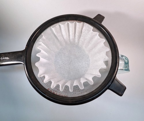 Coffee filter in a strainer over a large cup viewed from the top.