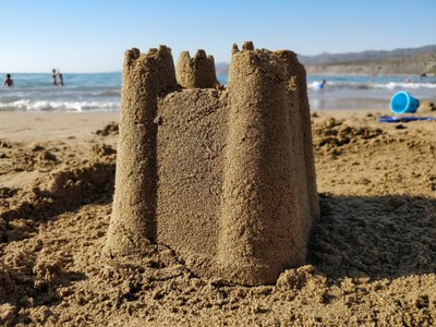 A single sandcastle on a beach, shaped from a bucket with four spires in the corners.