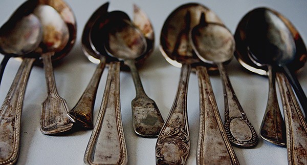 Twelve tarnished silver spoons appear dull and dirty