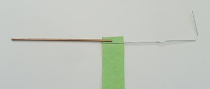 A paperclip is unfolded into an L shape and its longest side is taped to a nail sized iron core