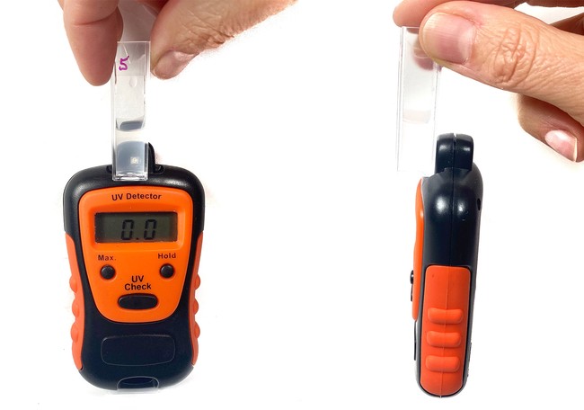 A hand holds a cuvette with liquid in front of the UV sensor of a UV meter.