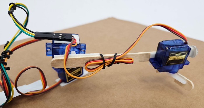 Side view of a robotic arm showing servo motor wires attached to the popsicle stick arm with twist ties so they are not loose