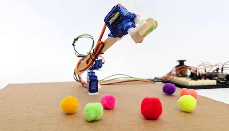 A robotic arm made with servo motors and popsicle sticks picking up a pom-pom