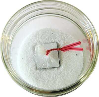 A square of magnetic tape wrapped in plastic is placed into a jar of salt and iron filings