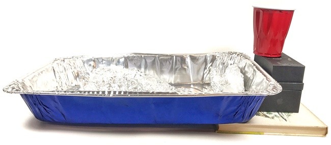 Inclined aluminum pan with the river model inside. A plastic cup is placed on top of boxes next to the aluminum pan, so that the water can flow from the cup into the aluminum river.