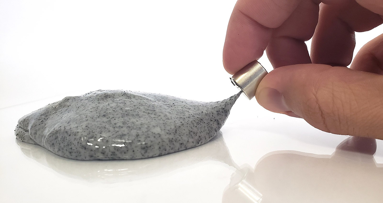A blob of gray slime. Fingers hold a magnet near the slime, and a small arm of the slime reaches up toward the magnet.