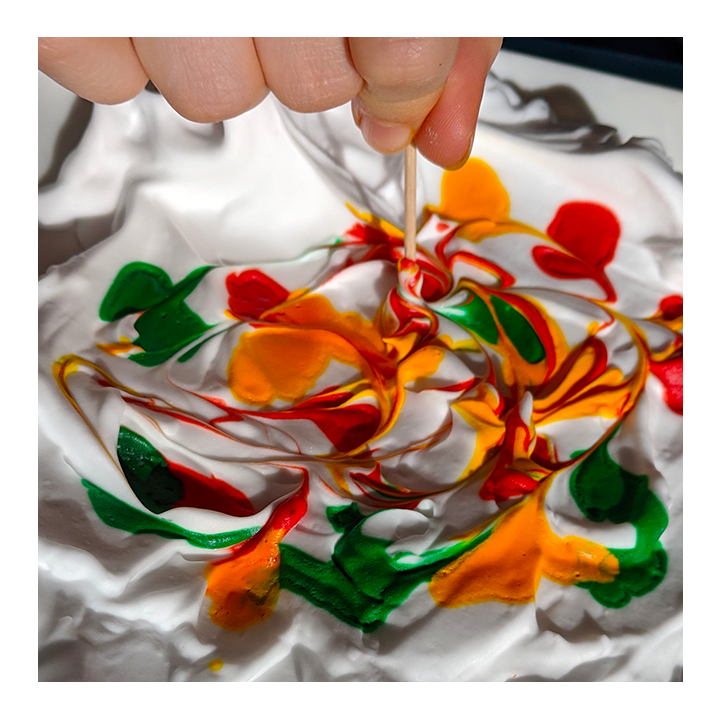 Example of food coloring swirled on top of shaving cream with a tooth pick as part of a paper marbling science activity - Awesome Summer Science Experiments