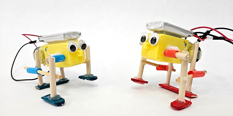 Two walking robots made from DC motors, wooden dowels, straws, and popsicle sticks
