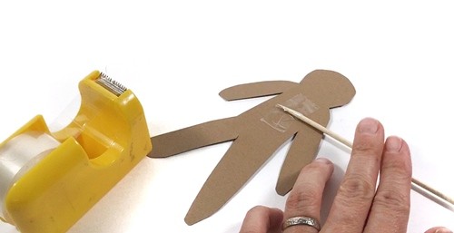 A wooden skewer is taped onto a cut out cardboard puppet.