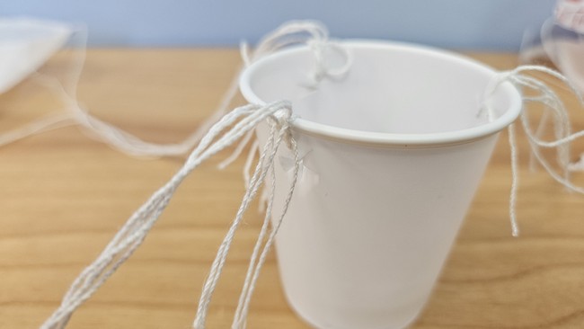 close up picture of plastic cup with strings from parachutes tied through holes around the rim