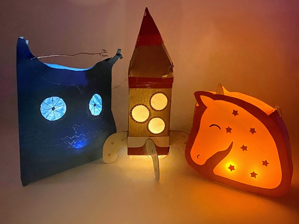 Three home-made paper lanterns including an owl, a rocket ship, and a unicorn.