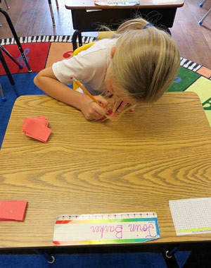 A student writes on a small square of paper while sitting at a desk