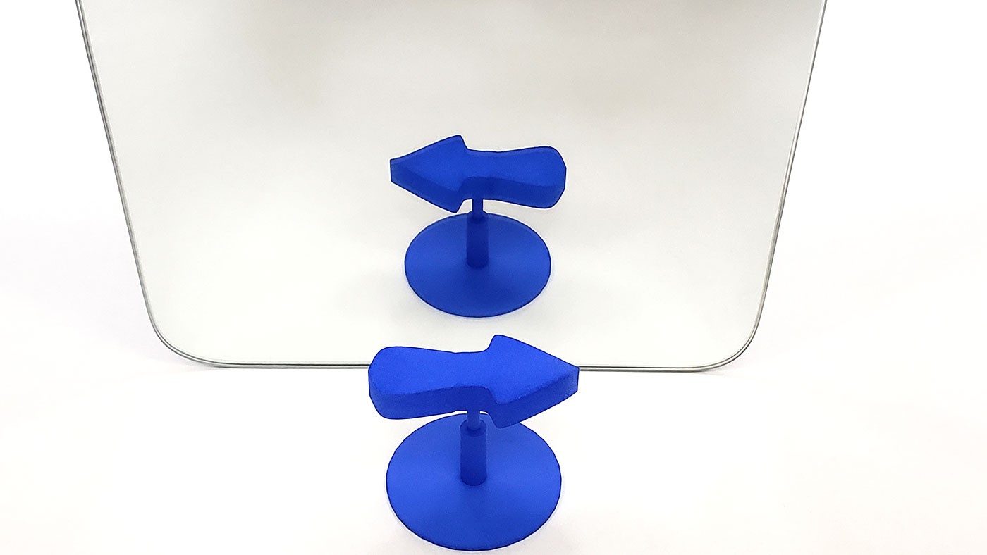A 3D printed arrow in front of a mirror. The arrow appears to point right, but its reflection appears to point left.