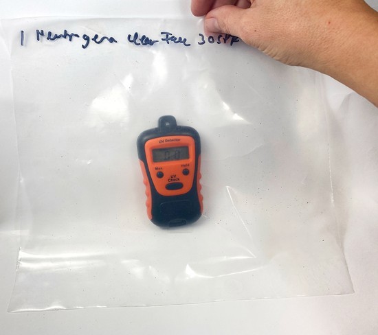 A hand holds a plastic sheet in front of a UV meter device.