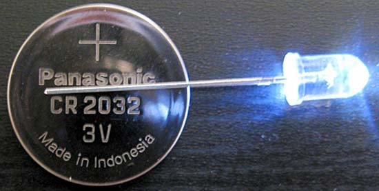 Coin battery inserted between the prongs on a white LED light bulb so that it remains lit