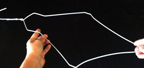 Hands holding a wire coat hanger that is diamond-shaped. 