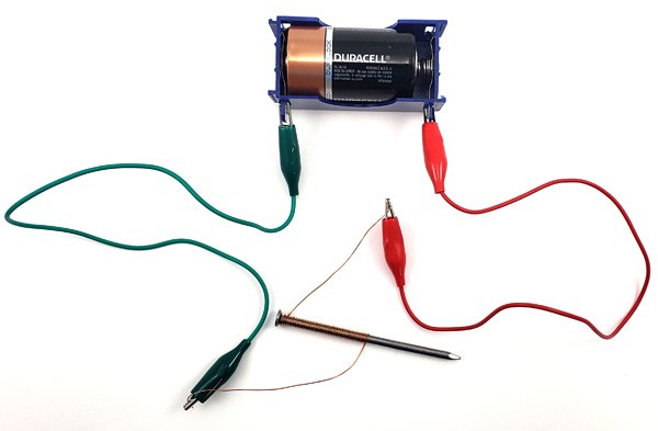Copper wire wraps around the body of a nail and is connected to a battery using alligator clips