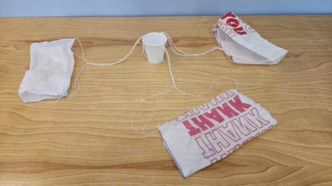 Plastic cup with three parachutes tied to it