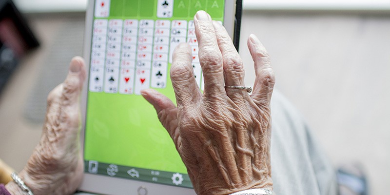 a wrinkled pair of hands playing a card game on a tablet